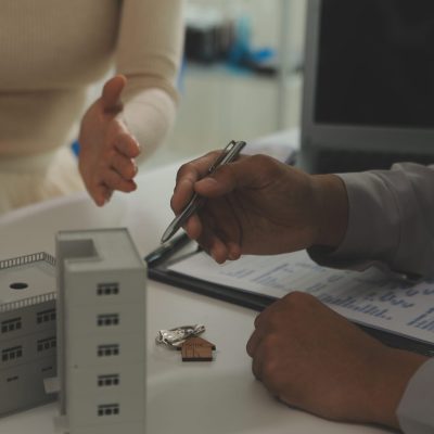 Real estate agent home sales broker is using a pen pointing to the house model and explains the business contract, rent, buy, mortgage, loan, or home insurance